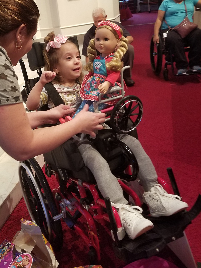 young girl in a red wheelchair with a doll